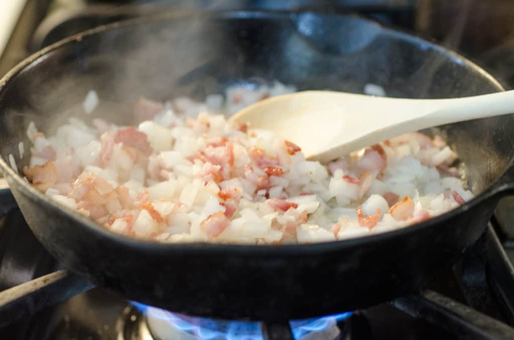 Chopped onion and bacon cook in a cast-iron skillet to make a Bacon Cheddar 30 Minute Skillet Strata - The Goldilocks Kitchen 