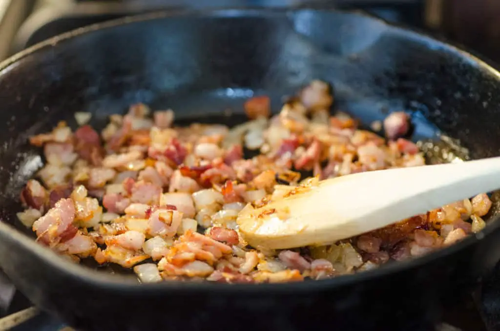 Chopped onion and bacon brown in a cast-iron skillet to make a Bacon Cheddar 30 Minute Skillet Strata - The Goldilocks Kitchen 