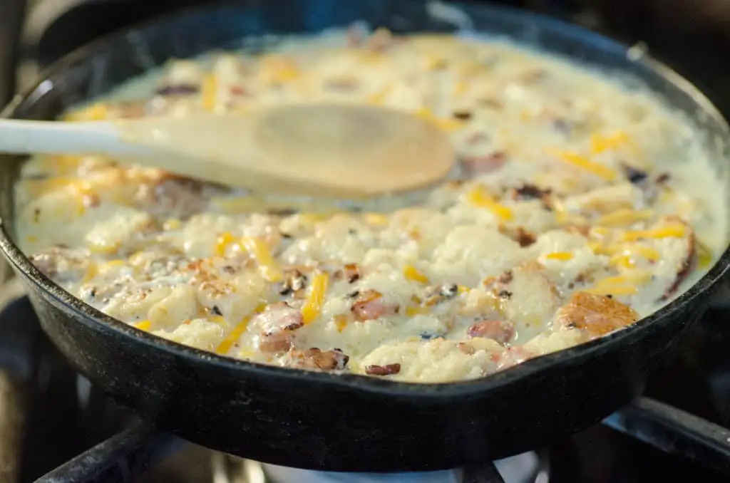 A mixture of uncooked egg, milk, bread, shredded cheddar cheese, chopped bacon and onion in a cast-iron skillet ready to be baked into a Bacon Cheddar 30 Minute Skillet Strata - The Goldilocks Kitchen 