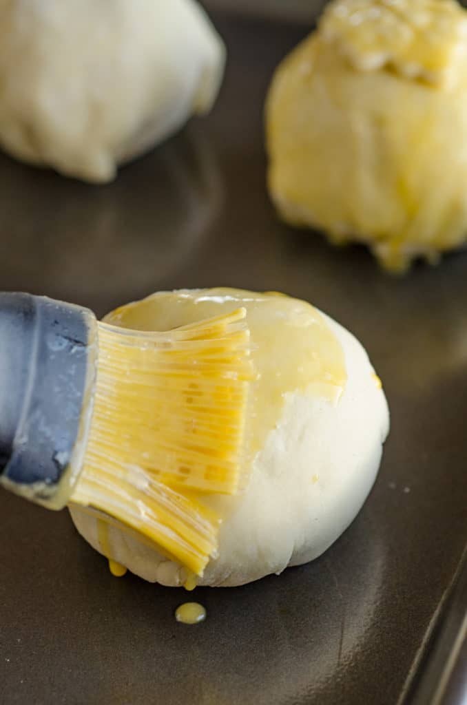 Beaten egg is brushed over a ball of dough (with a meatball inside) to make Easy Meatball Wellingtons - The Goldilocks Kitchen