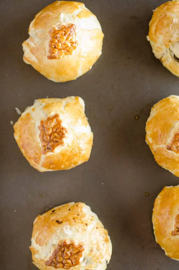 Freshy baked golden brown Easy Meatball Wellingtons sit in a row on a rimmed baking sheet. - The Goldilocks Kitchen