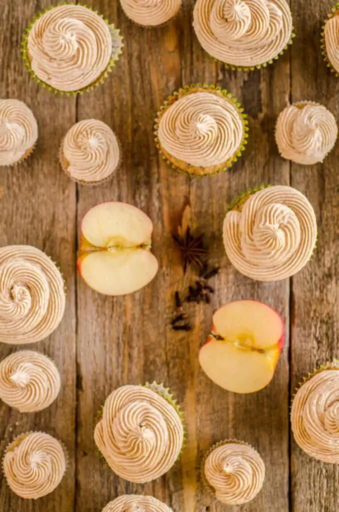 Apple Cinnamon Cupcakes from above on a wooden table; including regular sized and mini cupcakes, all with swirls of cinnamon buttercream frosting.- The Goldilocks Kitchen