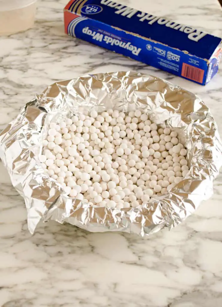 A raw pie crust is covered with aluminum foil and then filled with ceramic pie weights to show how to prebake a pie crust - The Goldilocks Kitchen