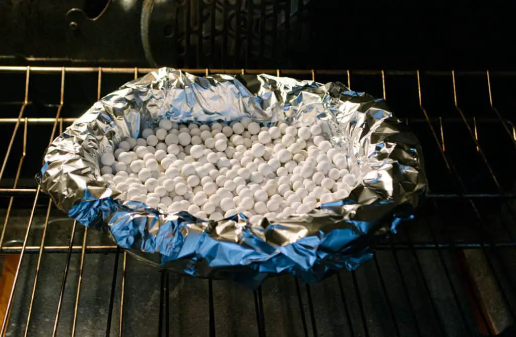 A pie crust blind bakes in an oven with ceramic weights to show how to prebake a pie crust - The Goldilocks Kitchen