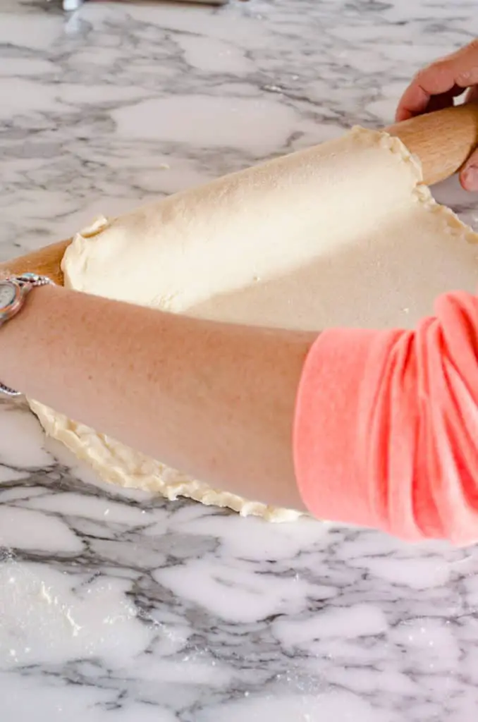 Pie dough is gently rolled onto a french rolling pin from off a counter to show how to prebake a pie crust - The Goldilocks Kitchen