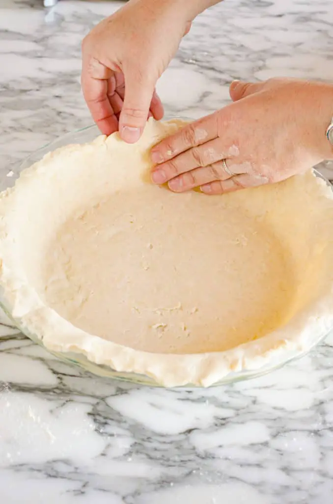 Dough for a pie crust is gently pressed into a pie plate to show how to prebake a pie crust - The Goldilocks Kitchen