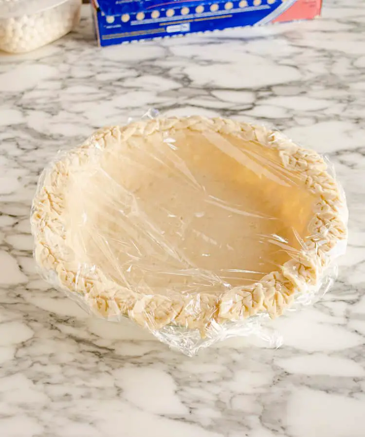 A pie plate filled with raw pie dough is covered with plastic wrap and frozen to set the dough in place to show how to prebake a pie crust - The Goldilocks Kitchen