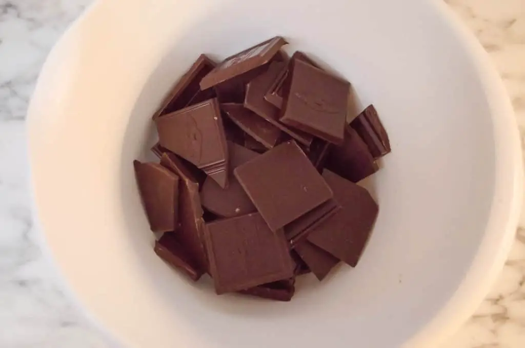Ghiradeli chocolate squares sit broken at the bottom of a white mixing bowl so they can be melted to make French Silk Pie without Raw Eggs - The Goldilocks Kitchen