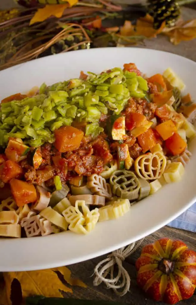 Green Chile Squash Goulash served over multi-colored pasta, piled into a large white oval platter.