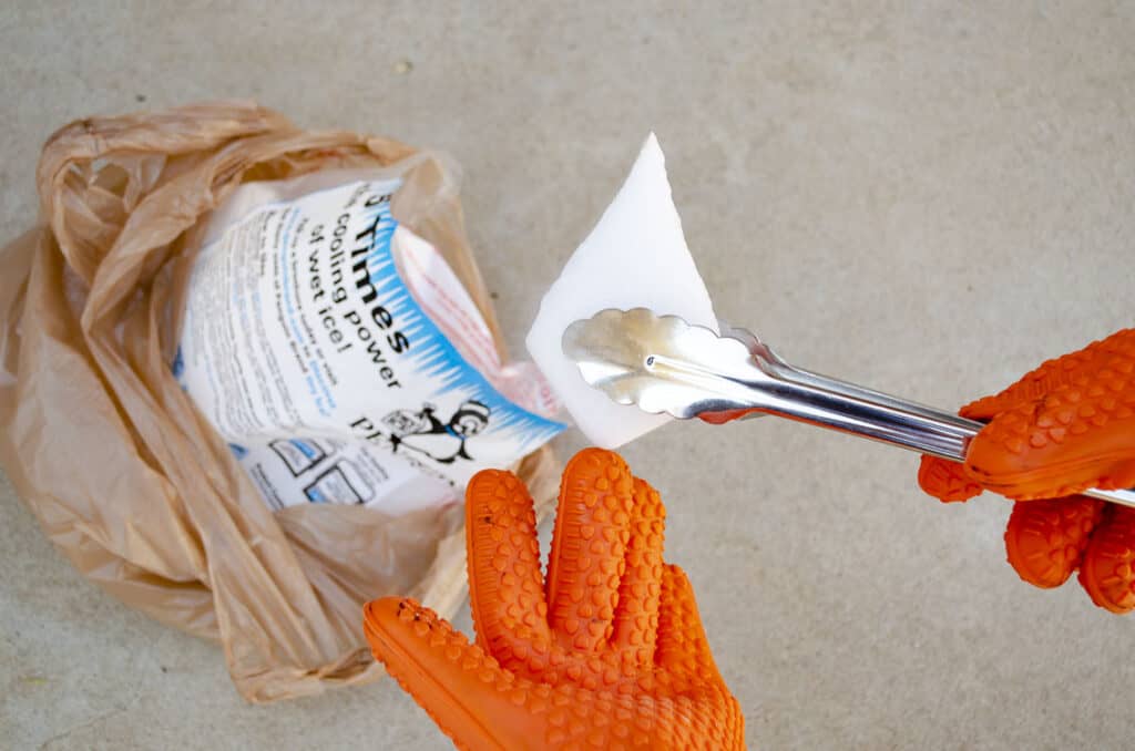 Metal tongs grab a piece of white dry ice from a bag of dry ice.