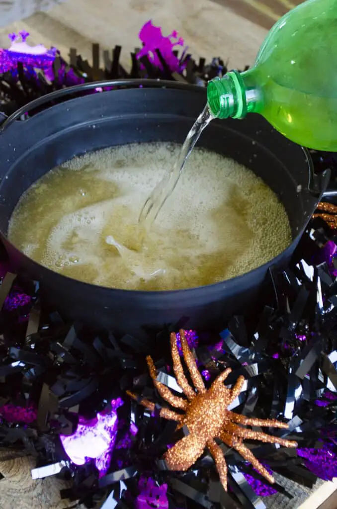 A bottle of ginger ale is being poured into a black plastic Halloween cauldron.