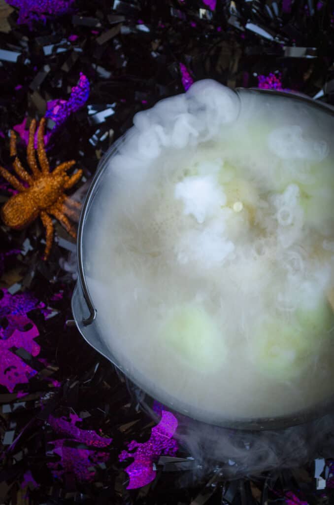 Looking down on a cloudy bubbly black cauldron with green liquid and lime green lumps of sherbert.