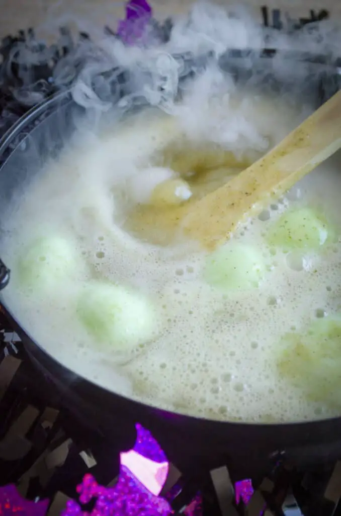 Witches Brew with Dry Ice with bubbles and steam in a black cauldron surrounded by Halloween decorations.