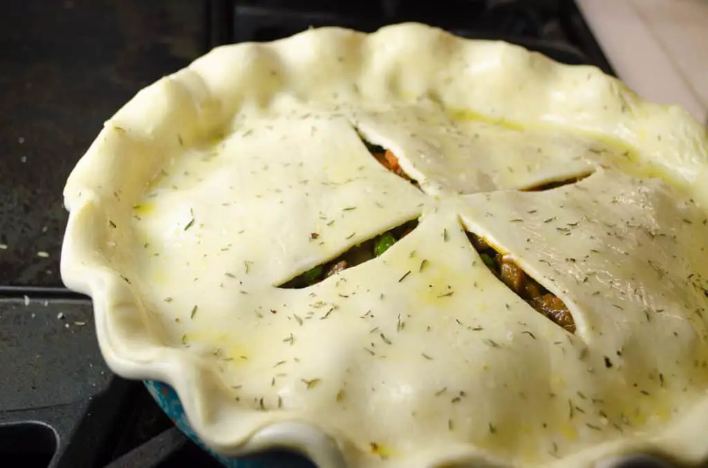 A pie crust brushed with beaten egg and cut with slits in the center is seasoned with salt, pepper and herbs.