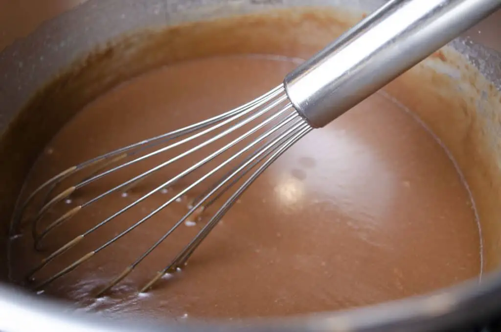A whisk stirs chocolate fudge in a large stockpot.