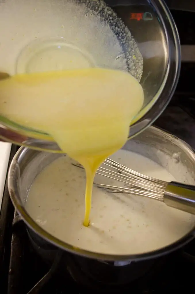 A yellow mixture of eggs and sugar is poured into a pot of hot milk and tapioca pearls to make Tapioca Pudding.