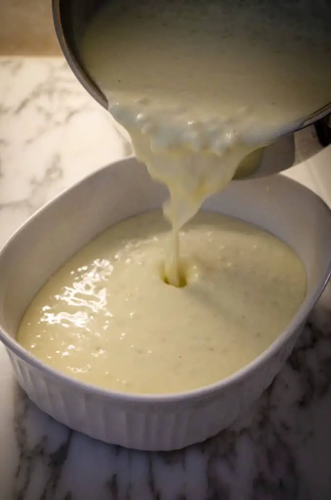 Tapioca pudding is poured from a pot into a white ceramic baking dish.
