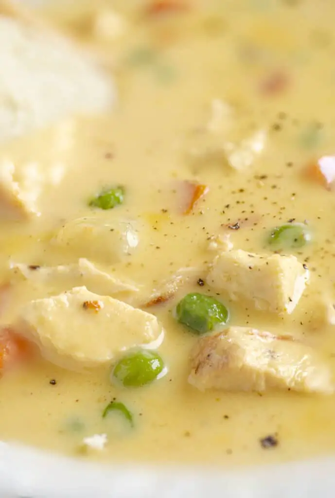 A close-up picture showing the tender chicken pieces, peas, carrots, potatoes suspended in a silky cheesy broth.