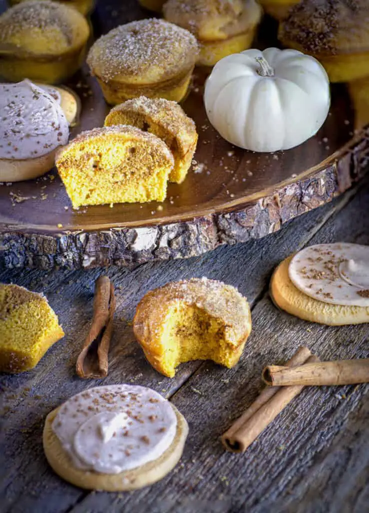 Snickerdoodle Pumpkin Muffins on a barn wood table surrounded by Snickerdoodle cookies, pumpkins and cinnamon sticks.