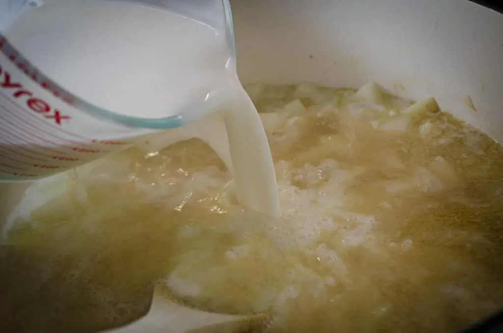 Milk is poured into broth and diced peeled potatoes to make Gluten-free Swiss Potato Soup.