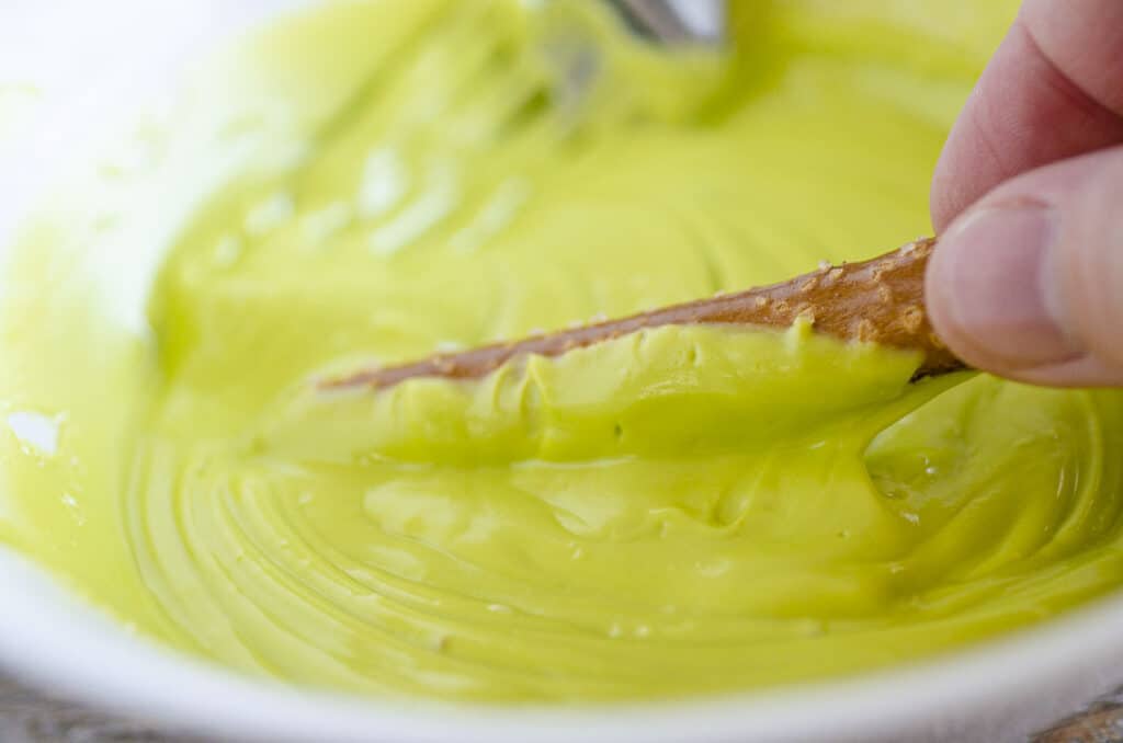 Closeup of green melted candy melts and a pretzel rod being dipped into and coated by the candy melt.