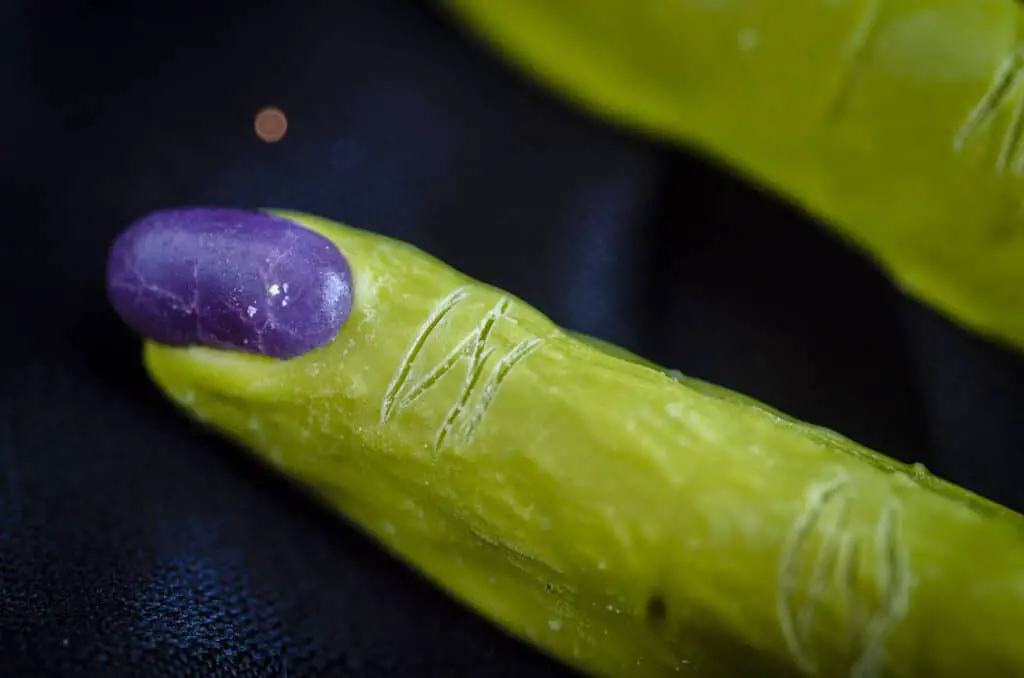 A closeup of a purple jelly bean 'finger nail' pressed into the candy melt-coated pretzel rod with lines drawn into the candy melt to look like knuckles.