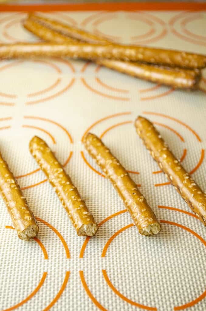 Broken pretzel rods laid out on a silicone baking mat.