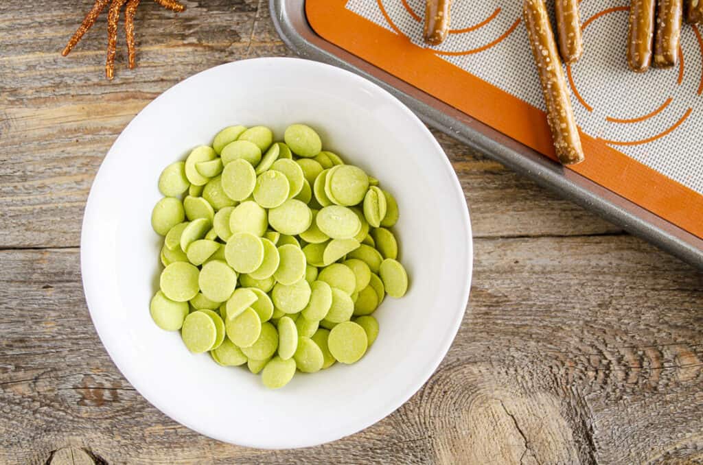 Looking down on a white bowl filled with green candy melts on a barn wood table.