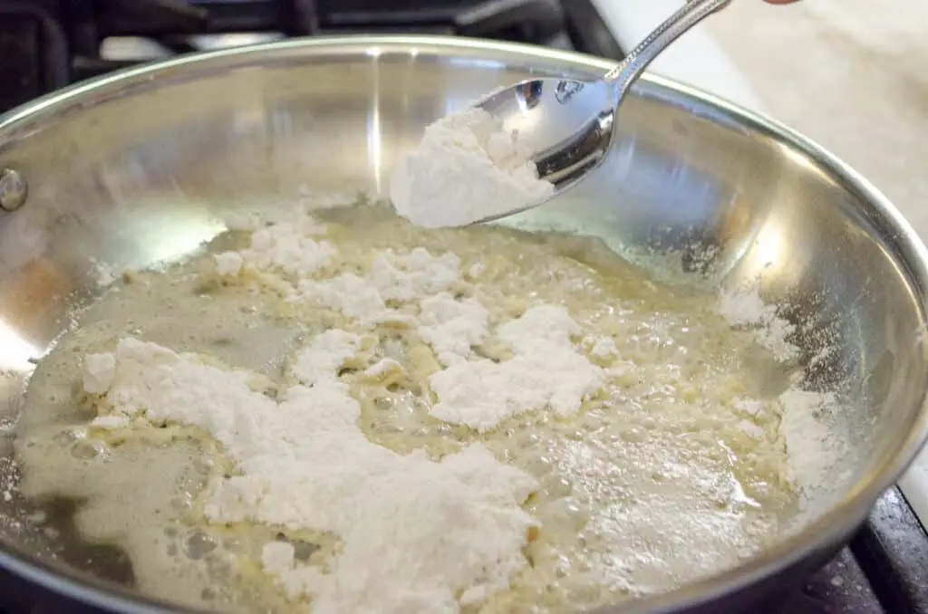 Flour is sprinkled over melted butter in a stainless steel saute pan.