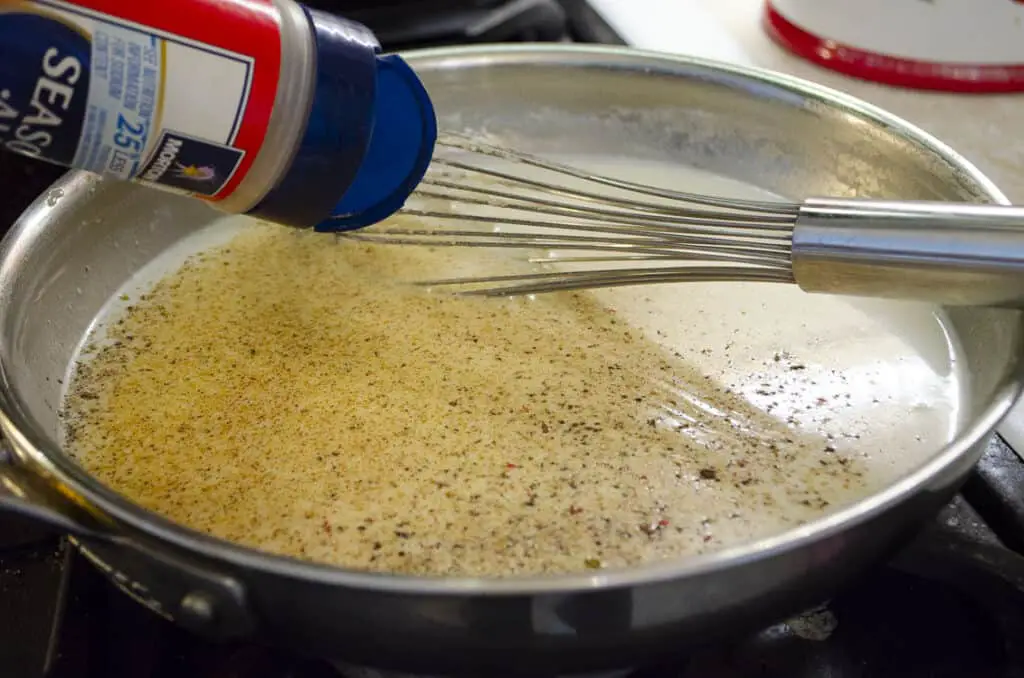 Seasoned salt is added to a mixture of milk, flour and butter in a saute pan to make Homemade White Country Gravy.