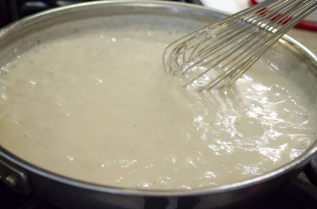 Homemade White Country Gravy boiling in a stainless steel saute pan.