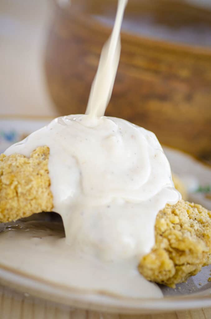 Homemade White Country Gravy is poured over fried chicken.