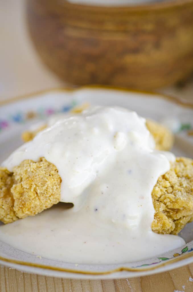 Golden fried chicken on a plate is smothered in Homemade White Country gravy.