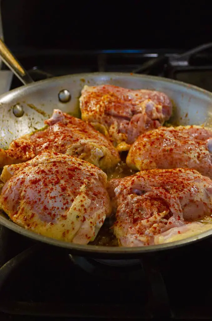 Bone-in, skin-on chicken thighs seasoned with paprika cook in a skillet.
