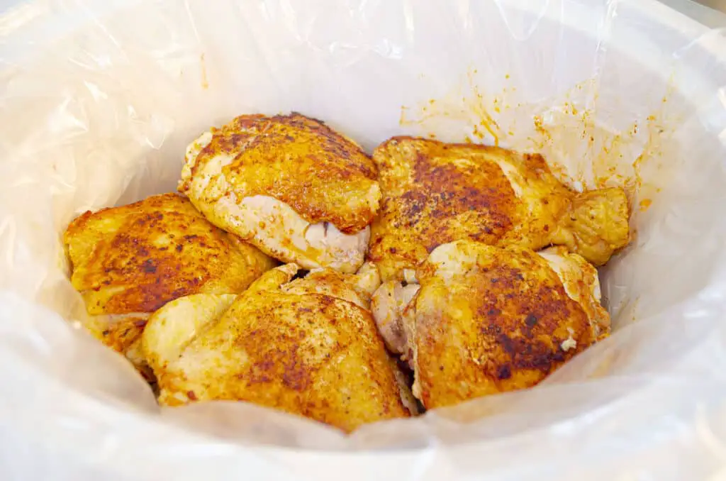 Browned chicken pieces nestled into the bottom of a slow cooker to make Slow-Cooker Brown Sugar Apple Chicken.