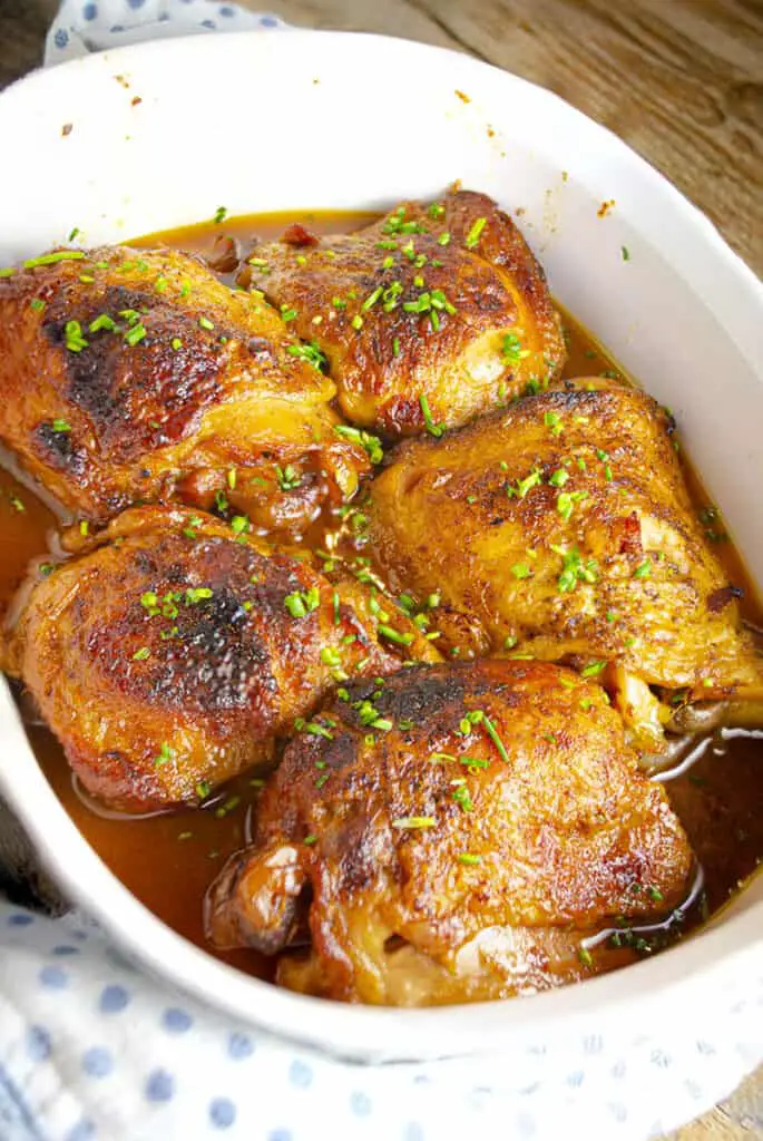 A white ceramic dish containing Slow-Cooker Brown Sugar Apple Chicken sprinkled with minced green chives.