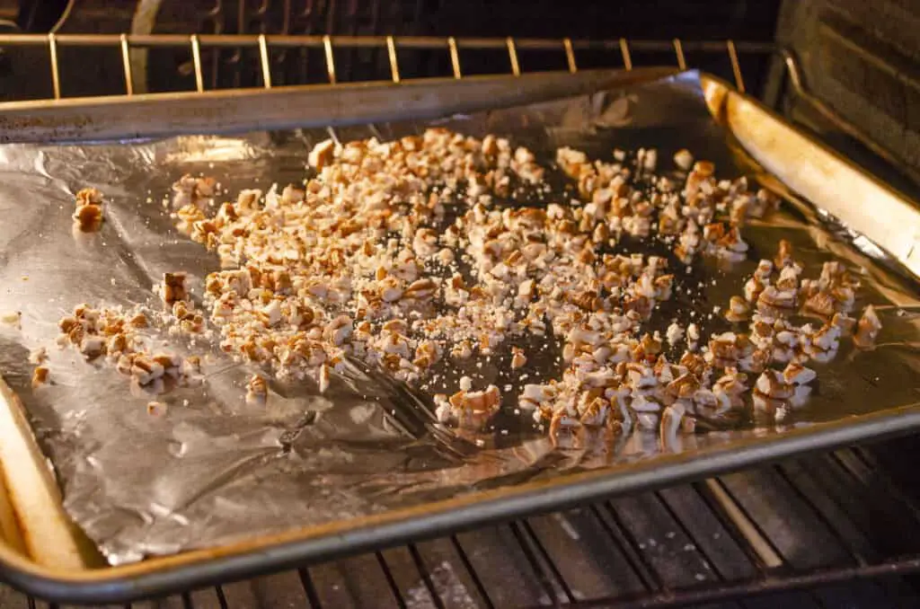 Chopped pecans in a rimmed baking sheet being toasted in an oven.