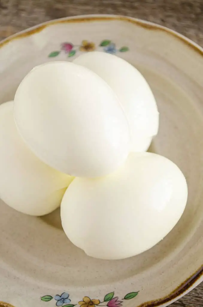 A few boiled and peeled eggs sit on a decorative plate.