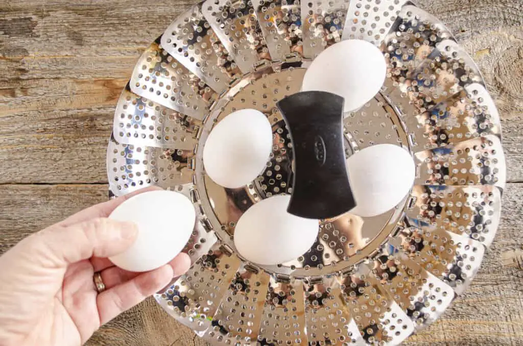 Raw eggs are placed into a metal collapsible steamer basket to make Easy-Peel Boiled Eggs.