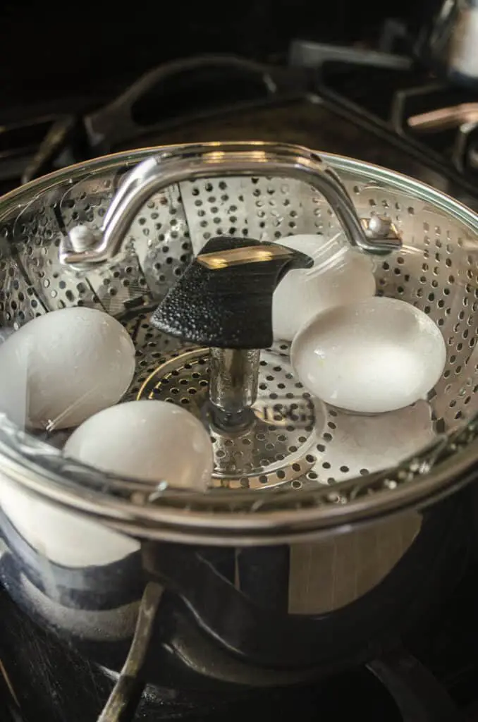 Eggs steaming in a steamer basked covered with a glass lid.
