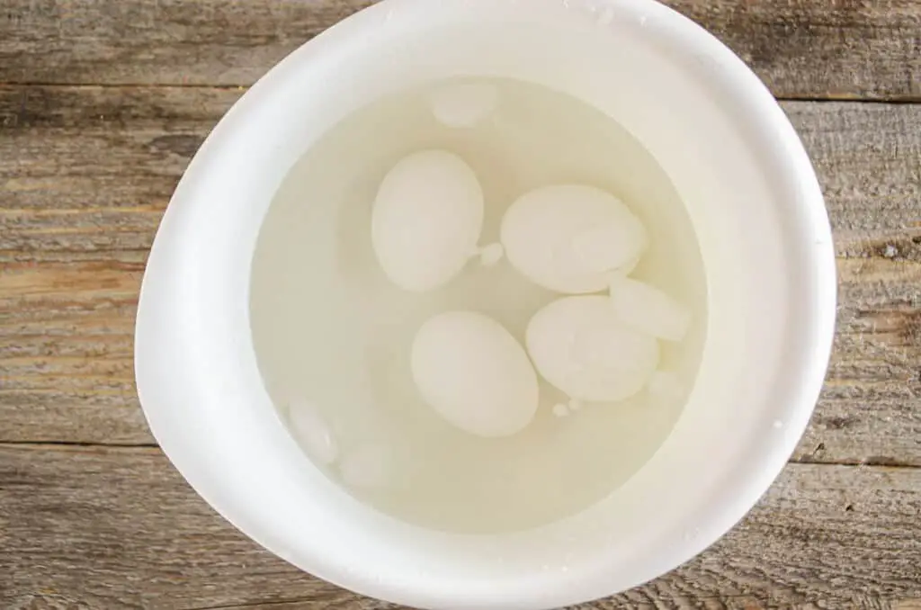 Boiled eggs soak in a bowl of ice water.