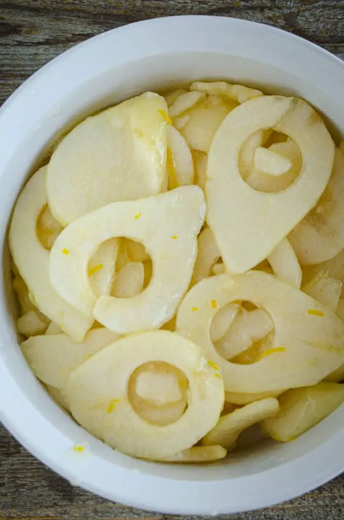 Sliced pears tossed with lemon zest, sugar and grated ginger fill a white round ceramic baking dish.