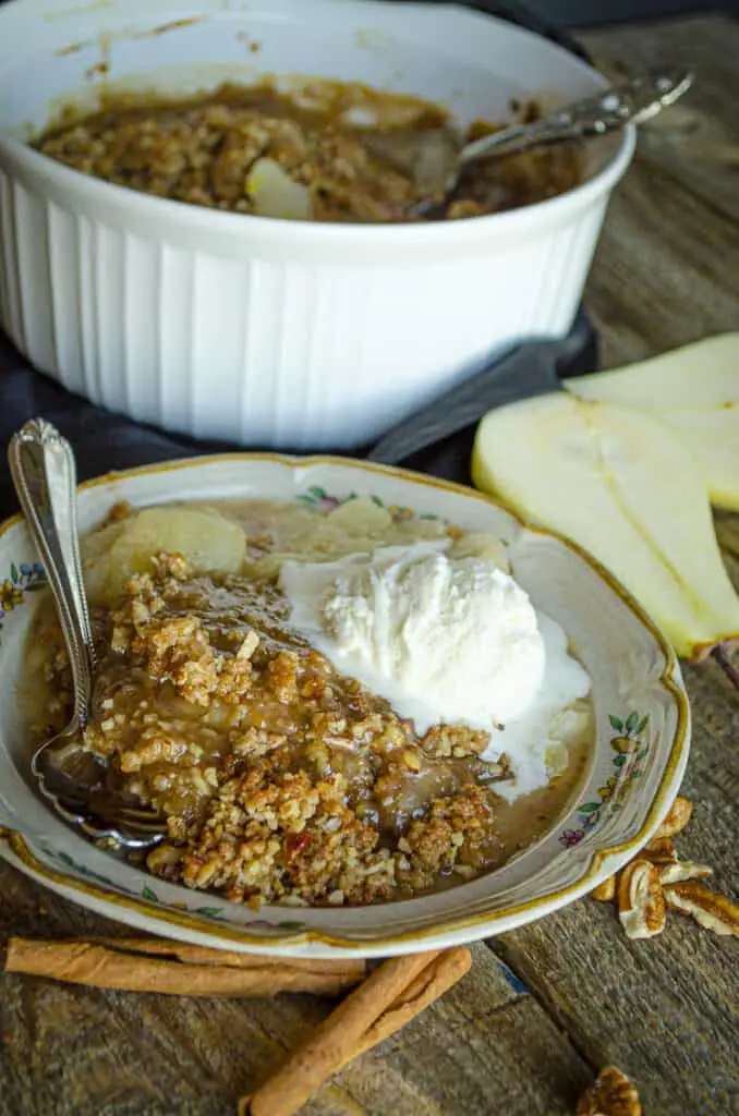 A closeup of a serving of Ginger-Pear Crisp showing the crumbly brown topping and thinly sliced cooked pears below.