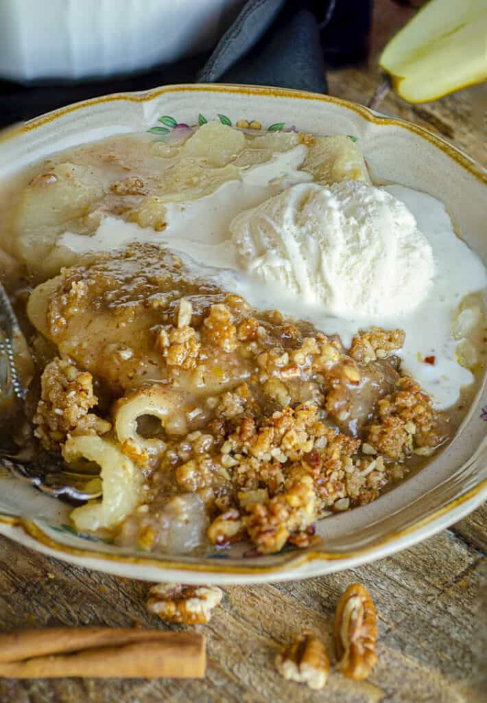 Ginger-Pear Crisp served on a plate and topped with melty vanilla ice cream.