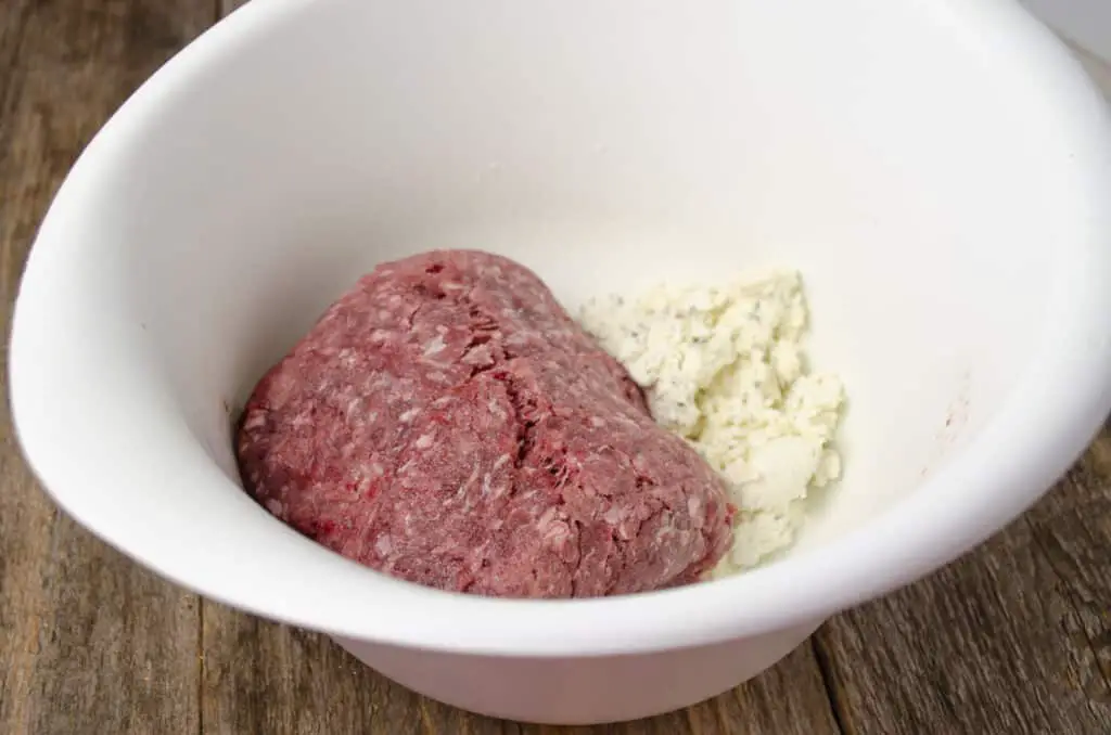 A white bowl contains ground beef and white Boursin cheese.