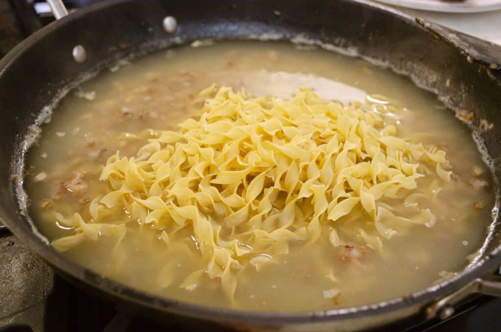 Dried curly egg noodles and chicken broth are added to a skillet to make One-Pot Meatball Stroganoff.