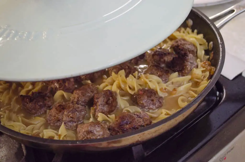 One-Pot Meatball Stroganoff in a large skillet is being covered with a lid to cook the noodles and meatballs together.
