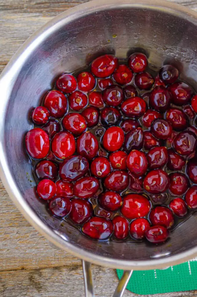 Bright red Cranberries covered in clear syrup in a small soup pot.