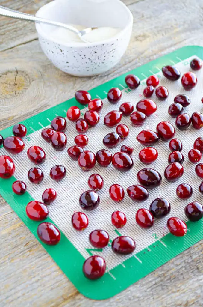 Cranberries coated in simple syrup cool on a silicone baking mat.