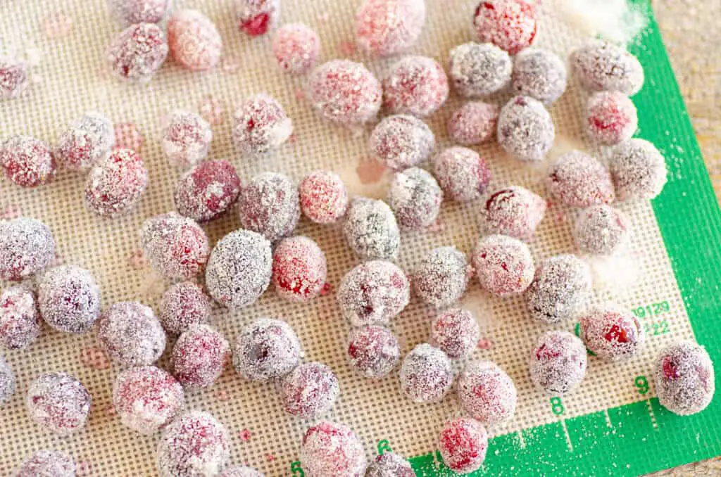 Sugared cranberries spread out on a silicone baking mat.